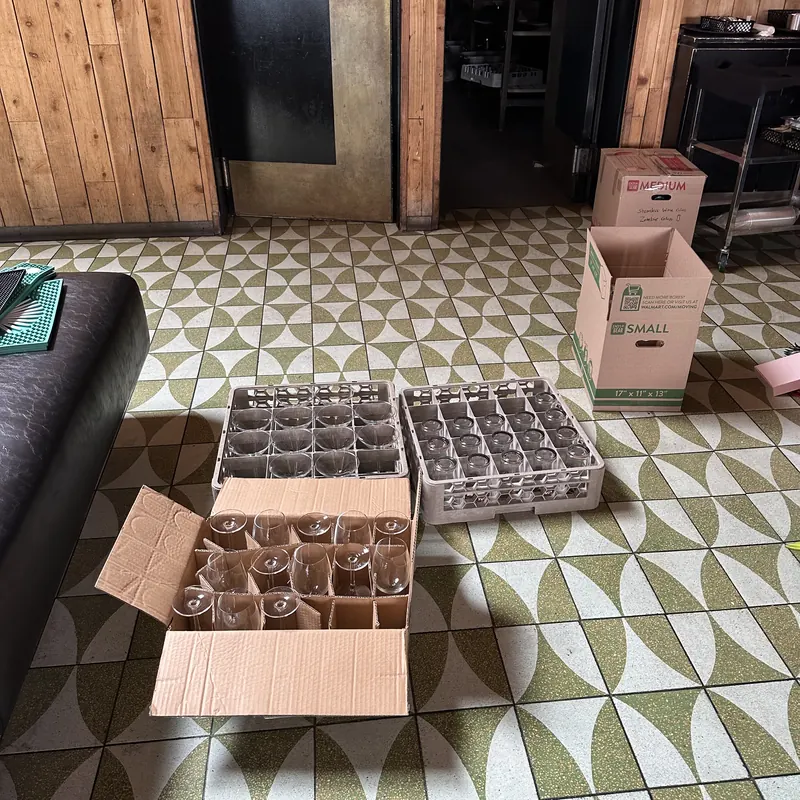 Crates of glassware and packed boxes staged on a tiled restaurant floor during a kitchen clean-out.
