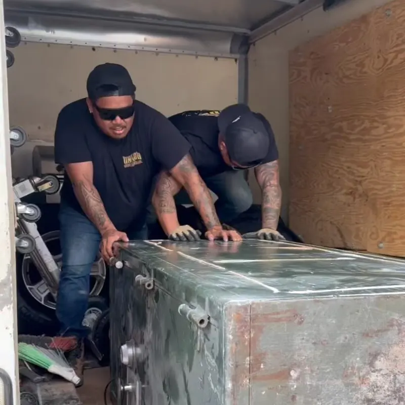 Two Unko's crew members sliding a large steel safe into the back of the box truck.